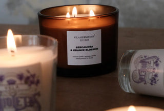 Velas artesanales encendidas sobre una mesa de madera, entre ellas la vela de bergamota y azahar de Vila Hermanos, hechas a mano en España con cera vegetal. Blog Real Fabrica Decorar con velas