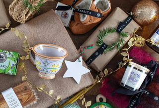 Composición navideña con regalos artesanos: manta, taza, zapatillas, jabón y decoración navideña de Real Fábrica.