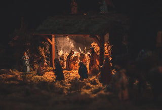 Misterio navideño con figuras del Belén bajo un portal de madera, iluminado suavemente en la oscuridad, evocando una escena íntima y sagrada.