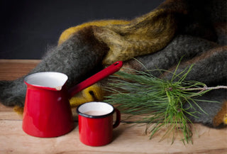 Manta de mohair artesanal acompañada de cafetera y taza de peltre rojas, símbolos de confort hogareño.