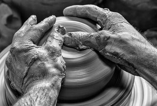 Manos de artesano moldeando una pieza de barro en torno de alfarero, símbolo del trabajo artesanal y del saber hacer tradicional.