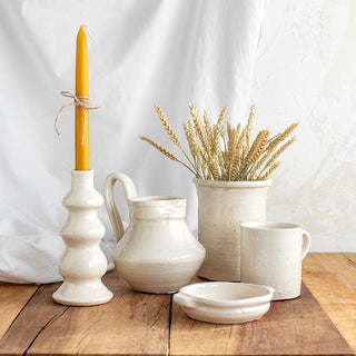 Vista de 5 piezas de cerámica artesana con acabado en esmalte blanco craquelado: candelabro con moldura, jarra con asa, portacubiertos, vaso con asa y cazuela de oreja cuadrada.