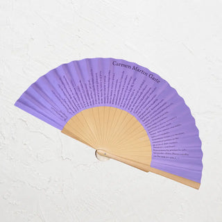abanico de algodón morado sobre fondo blanco con un fragmento del cuento "El cuarto de atrás" de Carmen Martín Gaite. Real Fábrica