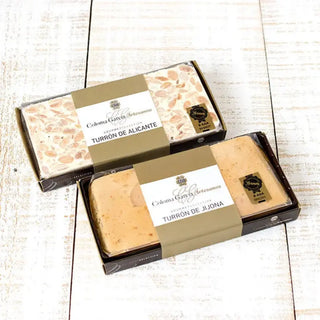 Foto mostrando un turrón de alicante y un turrón de jijona sobre una mesa de madera. Real Fábrica. 