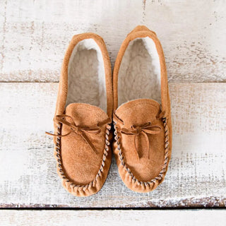 Foto cenital de unas babutxes kiova colocadas sobre una mesa rústica de madera, destacando su diseño cómodo, cálido y de estilo artesanal. Real Fábrica.