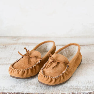 Foto frontal de unas babutxes kiova colocadas sobre una mesa rústica de madera, destacando su diseño cómodo, cálido y de estilo artesanal. Real Fábrica.