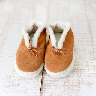 Foto frontal de unas babutxes de borreguito colocadas sobre una mesa rústica de madera, destacando su diseño cómodo, cálido y de estilo artesanal. Real Fábrica.