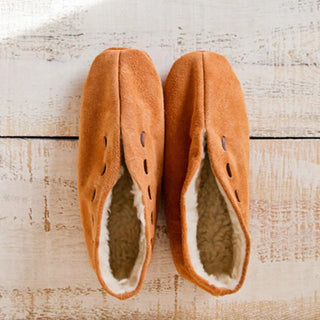 Foto cenital de unas babutxes Mallorquinas sin suela colocadas sobre una mesa rústica de madera, destacando su diseño cómodo, cálido y de estilo artesanal. Real Fábrica.