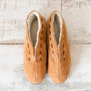 Foto cenital de unas babutxes Mallorquinas con suela de goma colocadas sobre una mesa rústica de madera, destacando su diseño cómodo, cálido y de estilo artesanal. Real Fábrica.