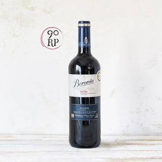 Una botella de Beronia descansa sobre una mesa de madera blanca, con su etiqueta elegante en tonos clásicos destacando en primer plano. Real Fábrica.
