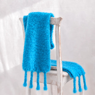 Bufanda chal de mohair azul cielo con flecos sobre una silla. Hecha en Excaray.