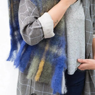 Una mujer toca con su mano la bufanda de mohair tartán de tonos azules que lleva al cuello, una fibra suave y de gran calidad desarrollada por Ezcaray, en la Rioja. Real Fábrica.