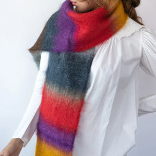 Foto de mujer abrigada con un suave y cálido foulard de franjas rojo,morado y mostaza. Real Fábrica.