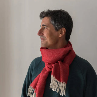 Foto de modelo de perfil mostrando los dos extremos y los flecos de la bufanda de lana merino en color roja. Real Fábrica