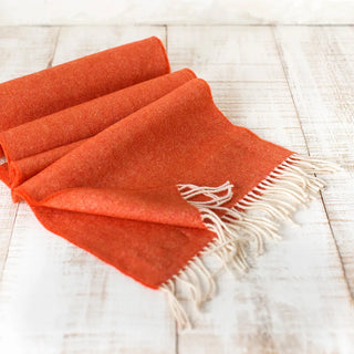 Bufanda expuesta sobre una mesa de madera, nuestras bufandas son elaboradas de lana merino, un tejido de alta calidad, suave, fino y transpirable.  Real Fábrica.