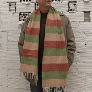 Foto de hombre luciendo nuestra bufanda de lana merino de rayas de color camel, jardín, y arcilla. Real Fábrica