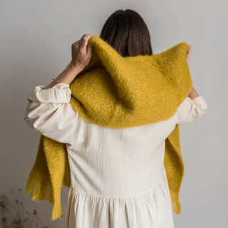 Foto de mujer de espalda con un foulard de mohair color amarillo, tejido a mano por los artesanos de Ezcaray. Real Fábrica.