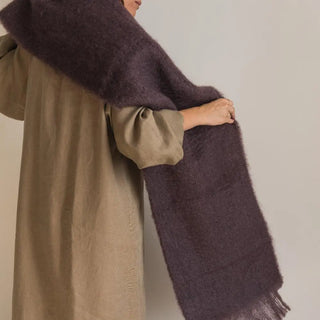 Foto de mujer de espalda luciendo nuestra bufanda de mohair de color berenjena en su hombro, tejido a mano por los artesanos de Ezcaray. Real Fábrica.