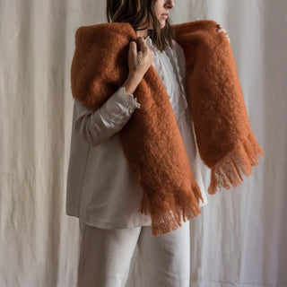 Mujer abrigada con una bufanda caldera, con sus manos contempla una fibra de origen natural ultra cálida y ligera, de gran calidad. Real Fábrica. 