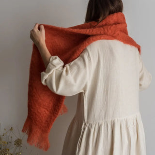 Foto de mujer de espalda luciendo una bufanda de mohair de color naranja en sus hombros, tejido a mano por los artesanos de Ezcaray. Real Fábrica.