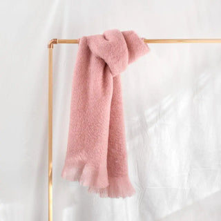 Bufanda de mohair hecha con lana riojana de color rosa, colgada sobre un perchero de madera. Real Fábrica. 
