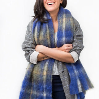 Mujer abrigada con una bufanda de mohair tartán azules, una fibra de origen natural ultra cálida y ligera, de gran calidad. Real Fábrica. 