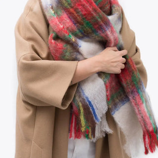 Una mujer de perfil  toca con su mano el foulard de mohair de tartán beige que lleva al cuello, una fibra suave y de gran calidad desarrollada por Ezcaray, en la Rioja. Real Fábrica.