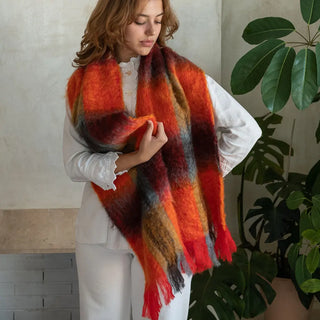 Foto de mujer abrigada con una suave y cálida bufanda tartán en tonos naranja y rojo. Real Fábrica.
