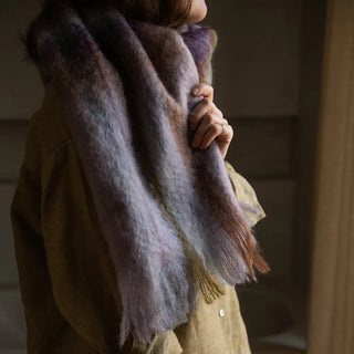 Mujer de perfil abrigada con una bufanda de mohair artesano de Ezcaray. Es de color tartán en tonos morado, verde y marrón. Real Fábrica.