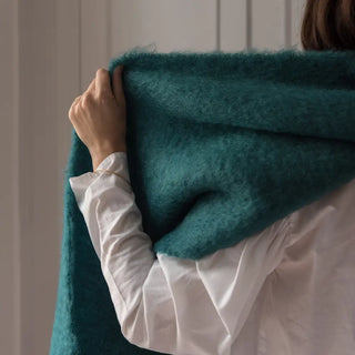 Una mujer de espalda toca con su mano la bufanda de mohair verde que lleva puesta, una fibra suave y de gran calidad desarrollada por Ezcaray, en la Rioja. Real Fábrica.