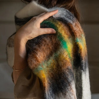 Mujer abrigada con un foulard de mohair tartán, una fibra de origen natural ultra cálida y ligera, de gran calidad. Real Fábrica. 