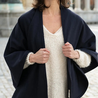 Foto de mujer tocando con sus dos manos los extremos de la capa de lana merino. Real Fábrica