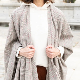 Mujer tocando con sus dos manos los extremos de la capa. Nuestras Capas de lana merino elaboradas con productos de calidad y manos ¡Artesanas y estilosas!. Real Fábrica