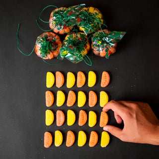 Paquetitos de naranjas y limones de caramelo. Gajos sobre fondo negro, colocados en forma damasquinada. Naranja de caramelo en Real Fábrica.