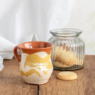 Taza de café de cerámica artesana en color amarillo y blanco junto con tarro de pastas. Real Fábrica