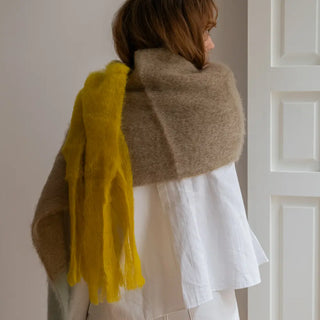 Foto de mujer de espaldas abrigada con un chal bufanda de mohair. Está confeccionado de manera artesanal en La Rioja. Real Fábrica.