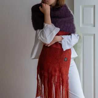 Foto de mujer envuelta en un chal tricolor de mohair tejido a mano. Es rojo, crudo y color berenjena. Real Fábrica.
