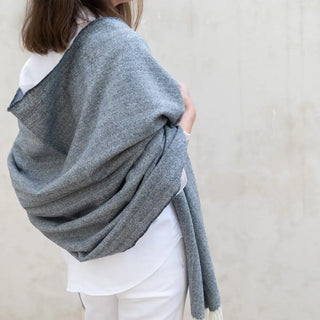 Foto de mujer de perfil luciendo nuestro Chal confeccionada en lana merina de la mejor calidad, de las ovejas de la Sierra de Grazalema, en Cádiz. Real Fábrica.