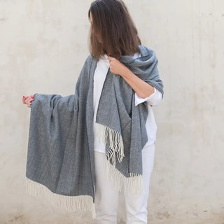 Foto de mujer mostrando los dos extremos de nuestro Chal de lana merino de Grazalema, con su tradicional acabado en flecos artesanos, es decir, que se anudan uno a uno y a mano. Real Fábrica.