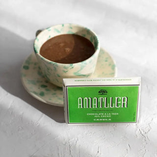 La foto muestra una taza de chocolate caliente junto a una tableta de chocolate de Amatller. Real Fábrica.