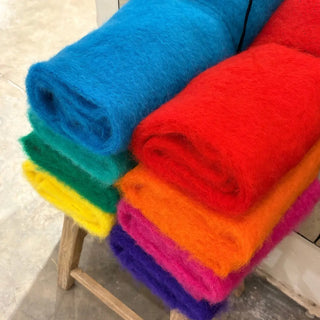 Bufandas de mohair de Ezcaray en varios colores apiladas sobre un taburete