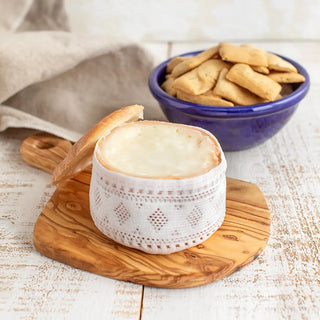 Torta de queso cremosito del Zújar abierto sobre una tabla de madera con un bol azul a su lado relleno de regañas. Real Fábrica. 