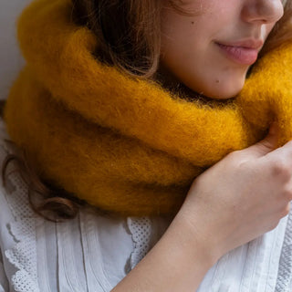 Primer plano de una mujer abrigada con un cuello de mohair en color mostaza. Se aprecia la primera calidad del tejido artesano. Real Fábrica.