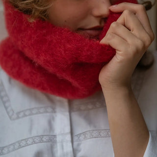 Mano de mujer acariciando la fibra suave y mullida de un cuello de mohair en color rojo. Está elaborado artesanalmente en La Rioja. Real Fábrica.