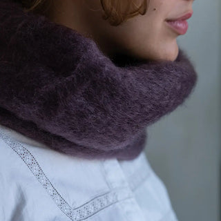 Foto de mujer abrigada con un cuello de mohair en color berenjena. El mohair es brillante, suave, ligero y muy cálido. Real Fábrica.