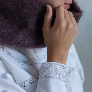 Mano de mujer agarrando el cuello de mohair berenjena que lleva puesto. En el primer plano se aprecia la suavidad y la calidad del tejido artesano. Real Fábrica.