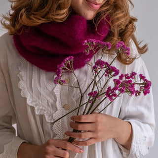 Una modelo posando con un cálido cuello de mohair. Sujeta un ramillete de flores del mismo color que el mohair, buganvilla. Real Fábrica.