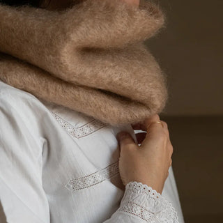 Mano de mujer agarrando el cuello de mohair camel que lleva puesto. En el primer plano se aprecia la suavidad y la calidad del tejido artesano. Real Fábrica.