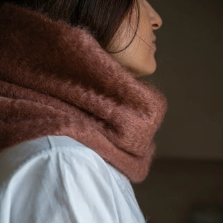 Foto de mujer de perfil abrigada con un cuello de mohair en tono canela. El mohair es brillante, suave, ligero y muy cálido. Real Fábrica.