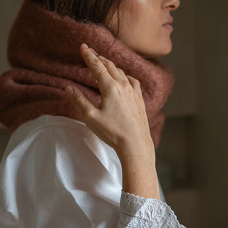 Mano de mujer agarrando el cuello de mohair canela que lleva puesto. En el primer plano se aprecia la suavidad y la calidad del tejido artesano. Real Fábrica.